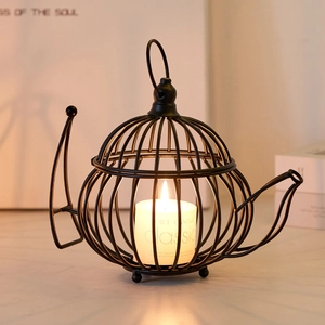 Nordic black iron teapot candle holder with a white pillar candle on a wooden table