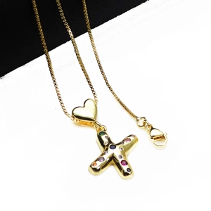 Detail view of a gold-plated necklace featuring a colorful zircon heart and X-shaped pendant