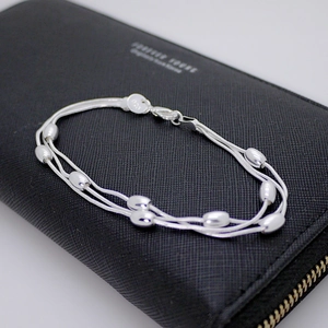 Detailed shot of silver triple-strand bracelet with olive beads on a black bag