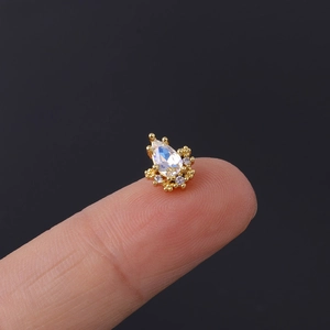 Macro view of tiny gold piercing stud with pear-shaped cubic zirconia on a fingertip