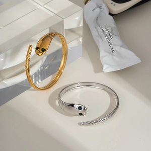 Detailed view of snake-shaped open bracelets in gold and silver with green gemstone eyes