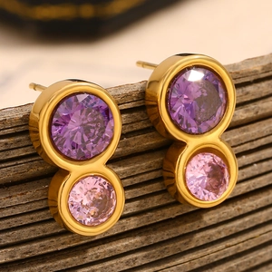 Detail of gold figure-eight earrings with purple and pink zircons on a wooden surface