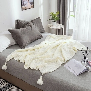 Close-up of white chunky knit throw blanket with decorative tassels on a cozy bed