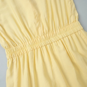 Detailed close-up of smocked elastic waistband on light yellow V-neck ruffle dress