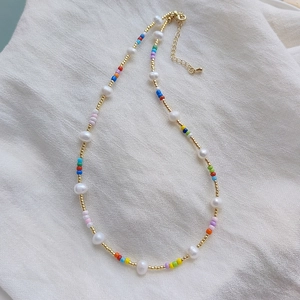 Colorful seed bead and freshwater pearl necklace with gold extension chain on white linen
