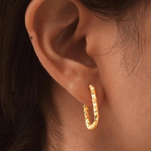 Macro shot of gold-plated stainless steel hoop earrings with textured diamond-cut pattern