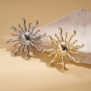 Minimalist sun-shaped metal brooches in gold and silver finishes on a stone display