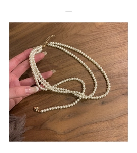 Close-up of layered pearl necklace with a gold heart pendant on a wooden surface
