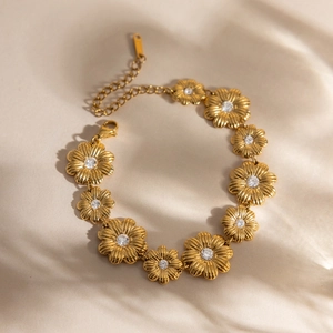 Detailansicht eines goldenen Gänseblümchen-Armbands mit Kristallen auf beigem Stoff