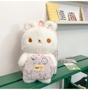 Detail of white plush bunny backpack with pink rabbit pattern pocket on a green bench
