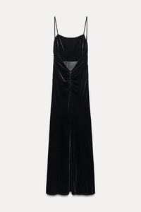 Detail of black velvet midi dress showing pleated texture and slim straps on grey background