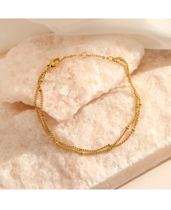 Close-up of double-layer gold bead chain bracelet on a decorative stone and fabric