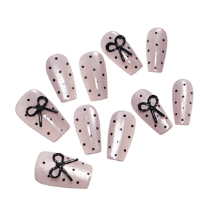 Press-on nails with pink base, black polka dots and 3D bow charms in a coffin shape