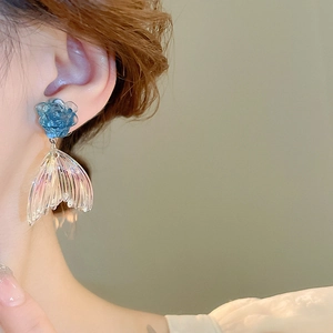 Close-up of blue acrylic flower and iridescent fishtail drop earrings worn by a model