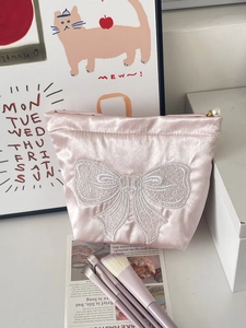 Detailed embroidery of white bow and pearl zipper pull on pink satin cosmetic bag
