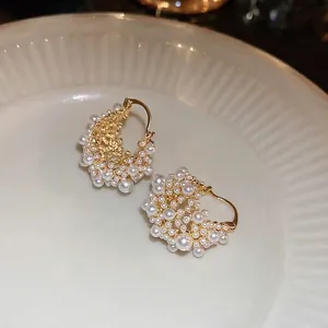 Elegant gold plated cluster pearl hoop earrings displayed on a white ceramic plate