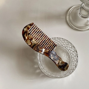Portable acetate hair comb with tortoiseshell pattern on transparent glass bowl