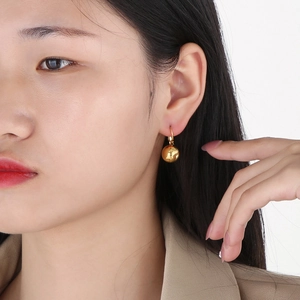 Close-up of a minimalist golden spherical earring on a female model with a polished finish
