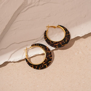Macro shot of tortoiseshell resin hoop earrings with golden metal borders on a stone surface