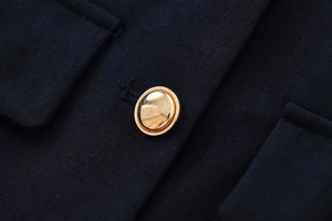 Close-up of golden embossed metal button on dark textured fabric of women's short jacket