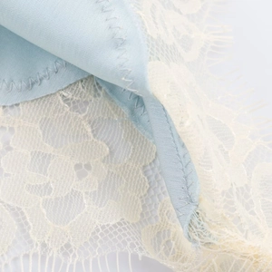 Macro detail of light blue satin fabric and off-white eyelash lace trim stitching