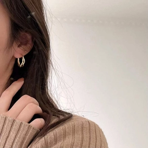 Close-up of elegant gold twisted double hoop earrings worn by a model in bright light