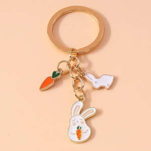 Detail of golden enamel keychain with white bunny holding carrot on pink background