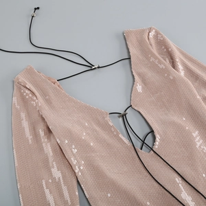 Detalle de vestido de lentejuelas oro champán con cuello en V y cordones negros