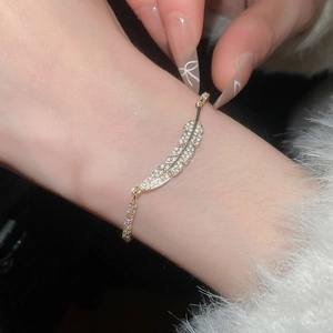 Detail of a gold feather bracelet with sparkling white zircons on a woman's wrist