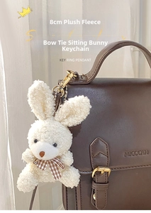 Close-up of a white plush bunny keychain with a plaid bowtie hanging on a leather bag