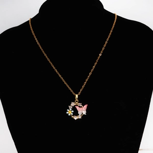 Détail du collier doré avec papillon rose, breloques florales et strass scintillants
