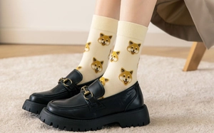 Detail of beige crew socks with Shiba Inu pattern worn with black horsebit loafers