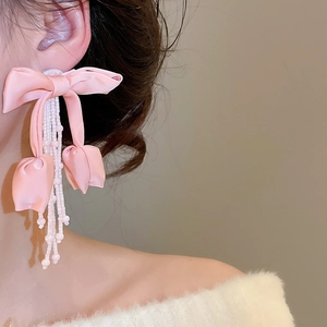 Detailed close-up of pink ribbon bow earrings with cascading white seed bead tassels
