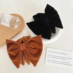 Close-up of velvet pearl bow hair claws in black and caramel brown on a wood tray