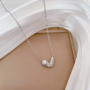 Detailed view of silver petal-shaped pendant on fine chain with soft fabric background