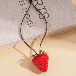 Close-up of realistic red strawberry pendant with green leaves and dark brown cord necklace