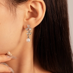 Boucle d'oreille pendante avec œil-de-chat en cœur, fleur en zircon et perle portée par un mannequin