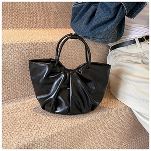 Detail of black glossy pleated cloud bag with soft leather texture on a beige rug