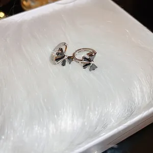 Detailed close-up of silver-tone bow earrings with black stones on white plush background