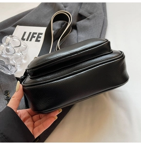 Close-up of black lychee grain crossbody bag with a striped wide shoulder strap
