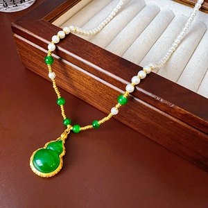 Détail d'un collier de perles vintage avec pendentif gourde verte sur plateau velours