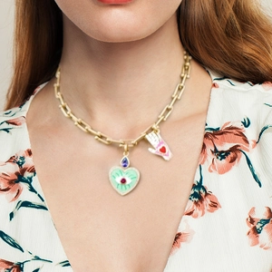 Detail of a gold T-bar necklace with heart evil eye and palm pendants on a model
