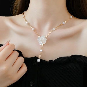 Close-up of elegant gold necklace with a large white flower pendant and hanging pearl