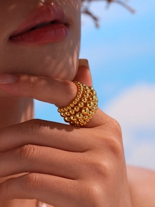 Close-up of golden multi-layered steel bead chain open ring worn against a blue sky