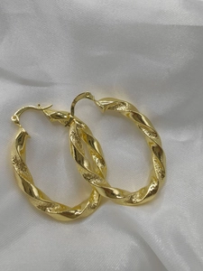 Detail of twisted gold metal hoop earrings with spiral texture on white silk fabric