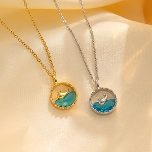 Detailed macro view of two minimalist whale necklaces with blue stones on warm gold satin.