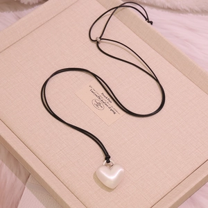 Detail of elegant heart-shaped pearl pendant on black cord over beige jewelry tray