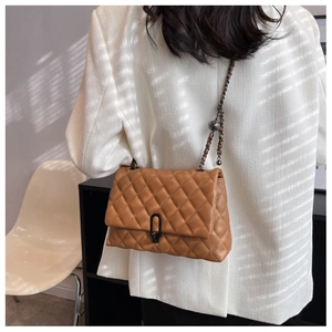 Brown quilted leather shoulder bag with dark metal chain strap worn on a white suit jacket