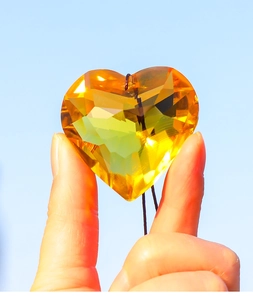 Macro detail of an amber heart-shaped crystal pendant held against a bright blue sky background