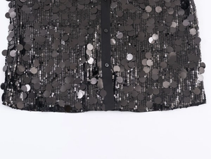 Close-up of black sequin blouse featuring round sequins and matching black button details